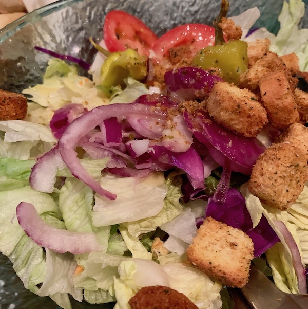 A bowl of salad with red onions, cabbage, and croutons