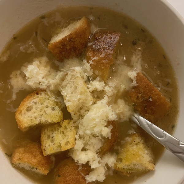 A bowl of fresh french onion soup topped with homemade croutons and shredded cheese