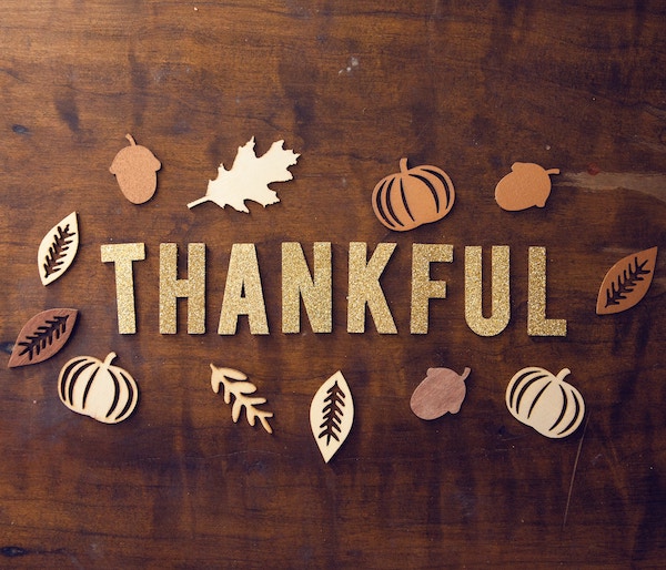 Artistic image of a wooden background that says Thankful surrounded by pumpkins and leaves