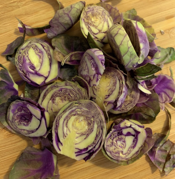 a pile of sliced purple Brussels sprouts that are a tie dye of purple, yellow, and green on a bamboo cutting board