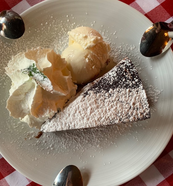 a piece of dark chocolate cake on a white plate with a scoop of vanilla ice cream, topped with whipped cream