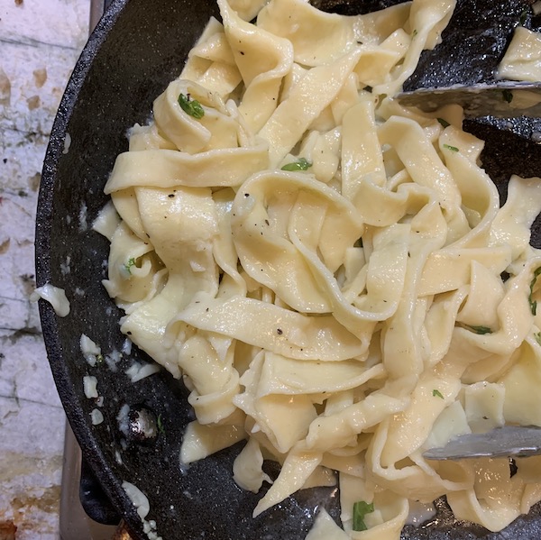 Cast iron skillet with fresh pasta and herbs on a marble counter top