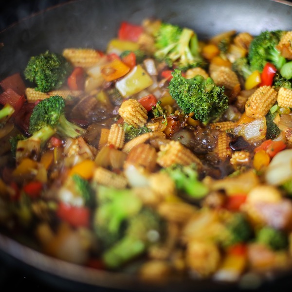 A rainbow of vegetables being sauteed in a pan with stir fry sauce.