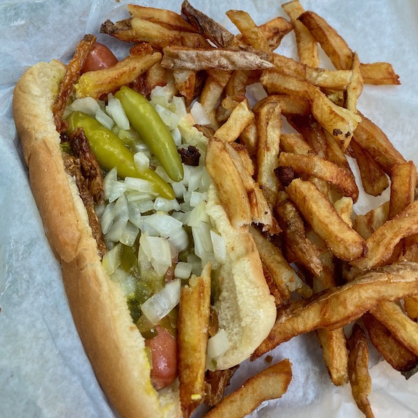 A hot dog with onions, spicy peppers, and relish with a side of crispy french fries